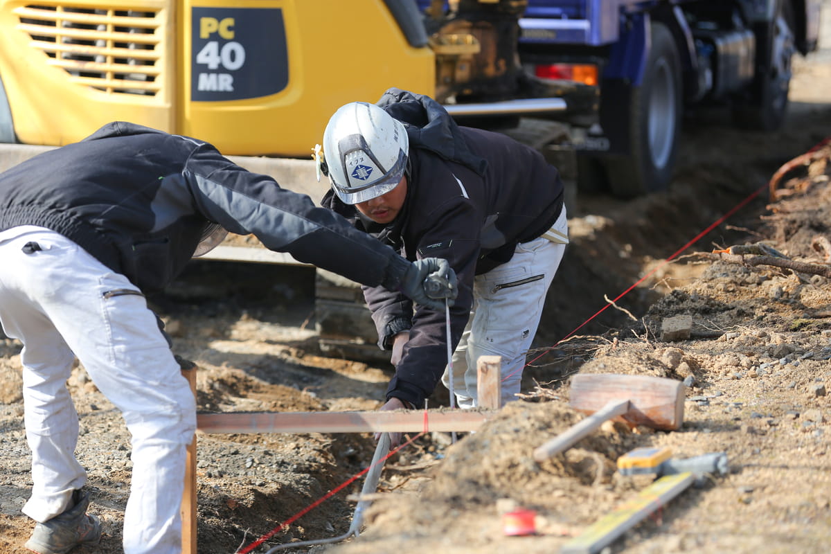建設現場でヘルメットを着用した作業員が、測定器具を使って地面のレベルを調整している
